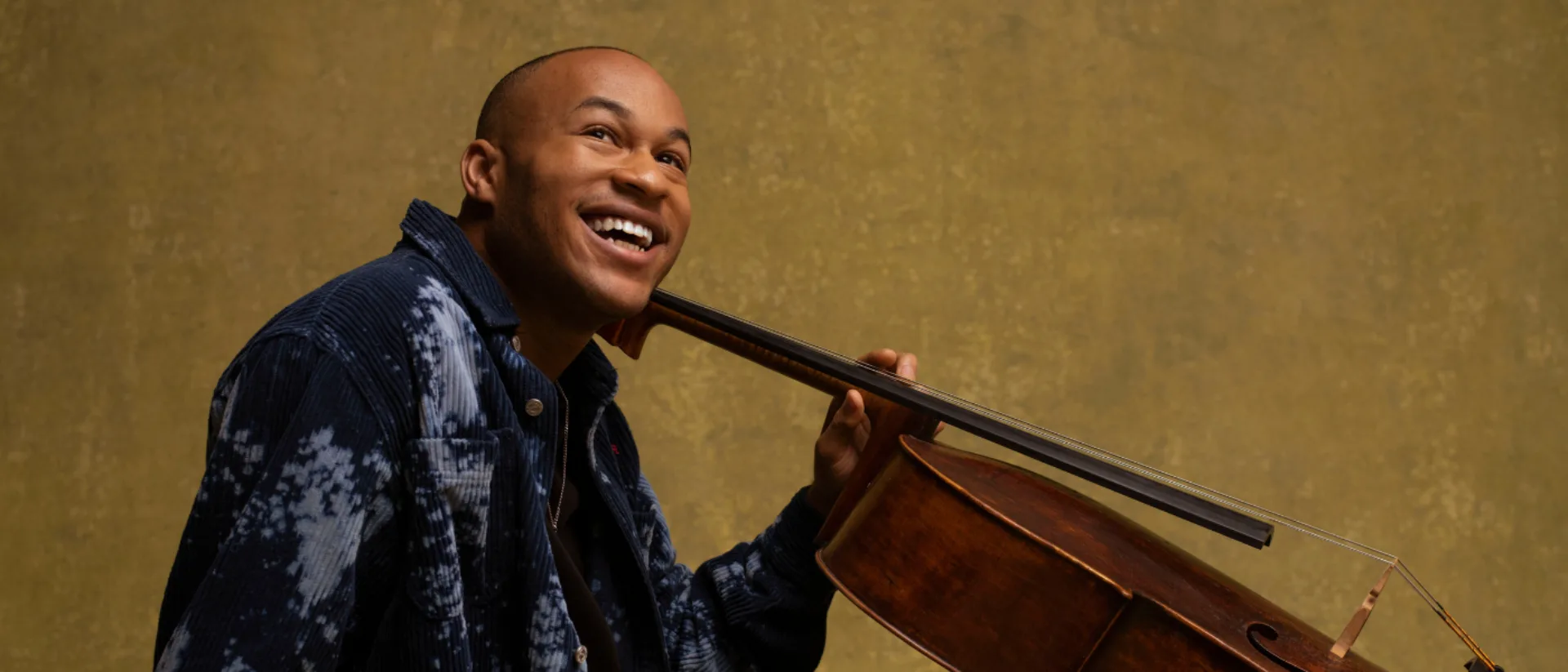 A man smiling looking up, holding a cello