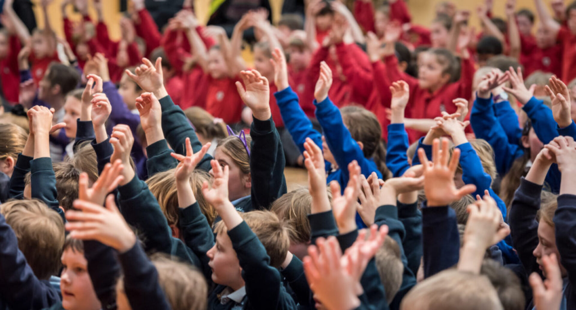 Children in colourful primary school uniforms raise their hands