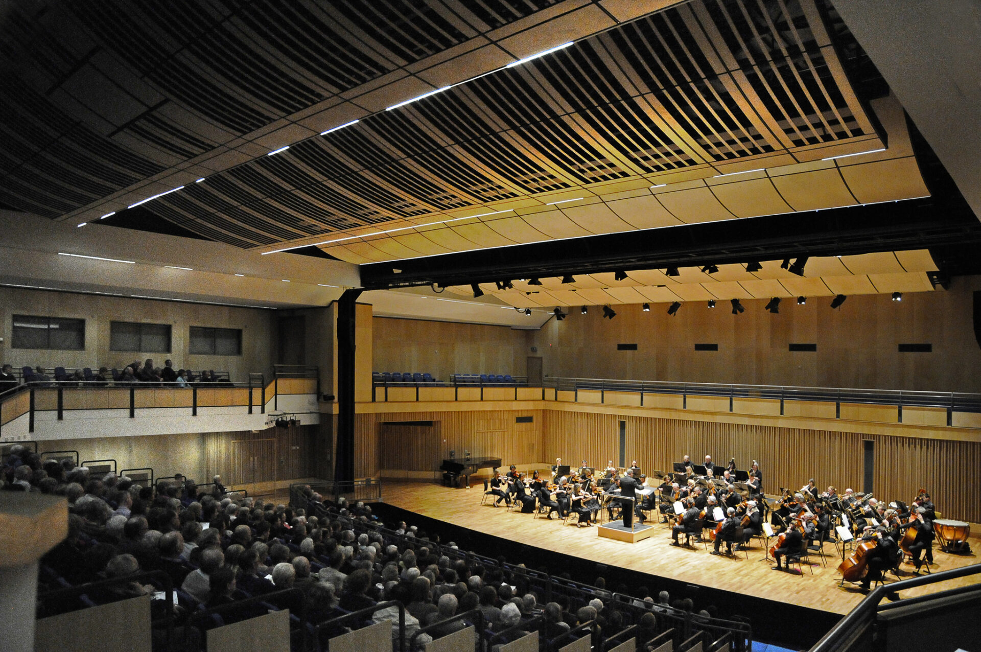 Side view of the wooden-clad auditorium with the audience sat in tiers in front of a performance from school musicians