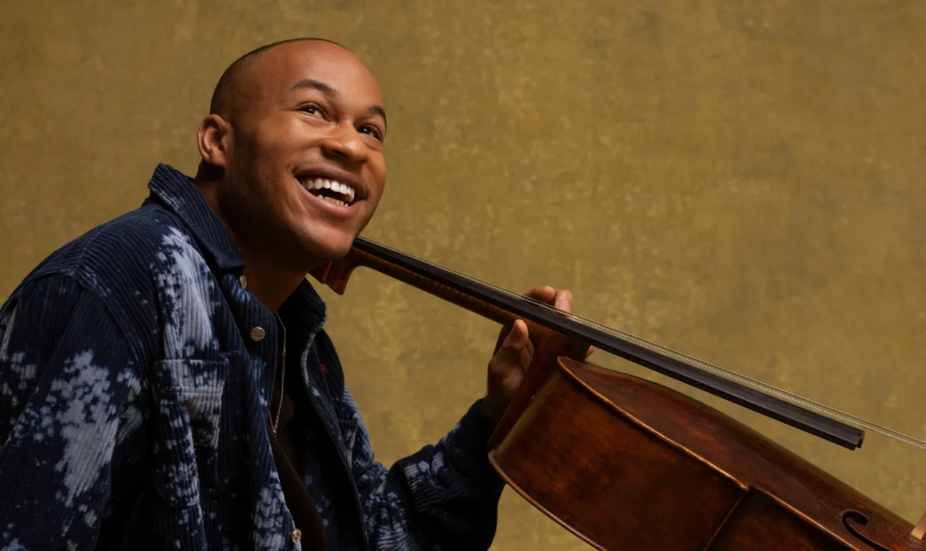 A man smiling looking up, holding a cello