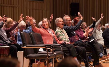 A group of seated older people hold are waving, doing actions and singing